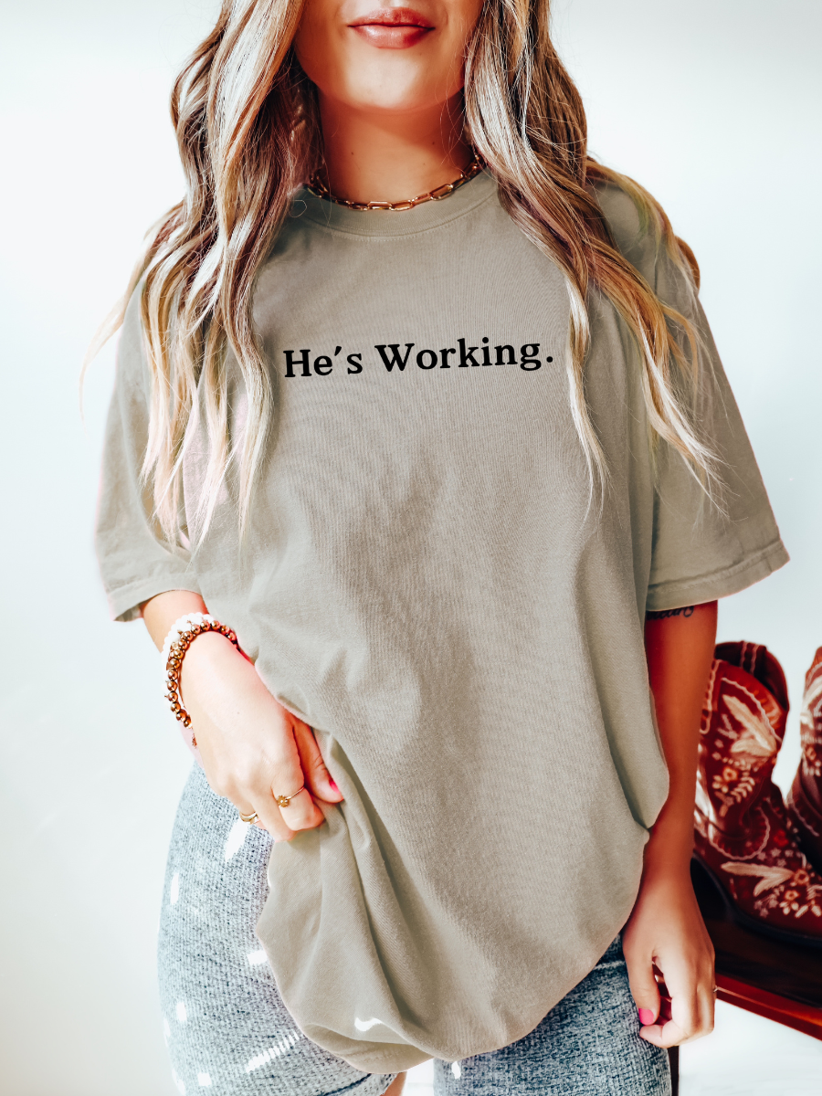 HE'S WORKING. - ADULT TEE